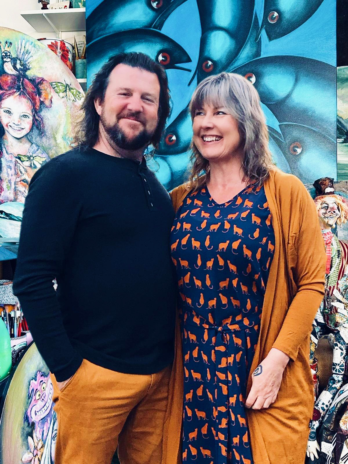 Glenn and Claire laughing together in their art studio, surrounded by paintings